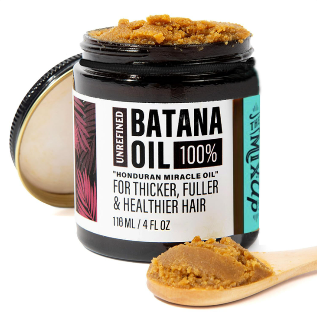 Open jar of the BatanaBloom™ batana oil hair mask with its lid and a wooden spoonful of paste