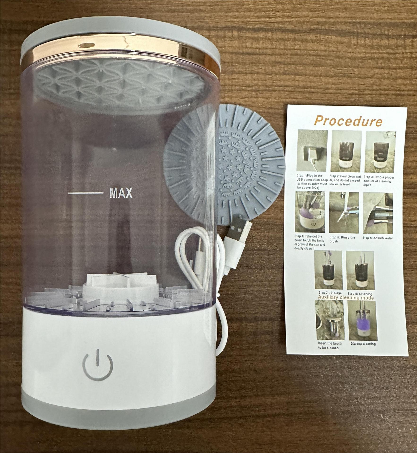 SwiftClean™ electric makeup brush cleaner with clear cylinder, USB cable, and instruction card on a wooden surface