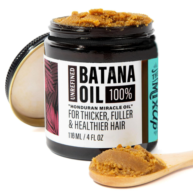 Open jar of the BatanaBloom™ unrefined batana oil hair mask with a wooden spoon of the rich brown paste